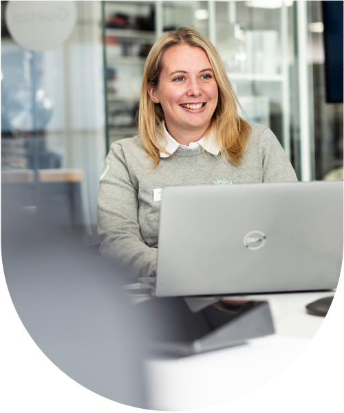 Kvinnlig Voky-anställd sitter vid ett skrivbord med en dator och ler