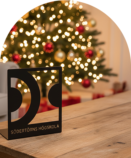 En svart bokstöd med Södertörns högskolas mönster står på ett bord framför en suddig julgran.